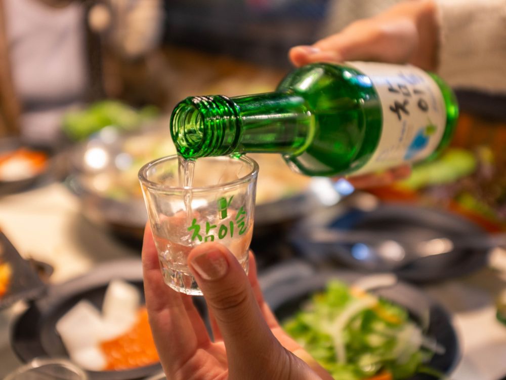 Imagem de uma pessoa servindo uma dose de Soju Coreano